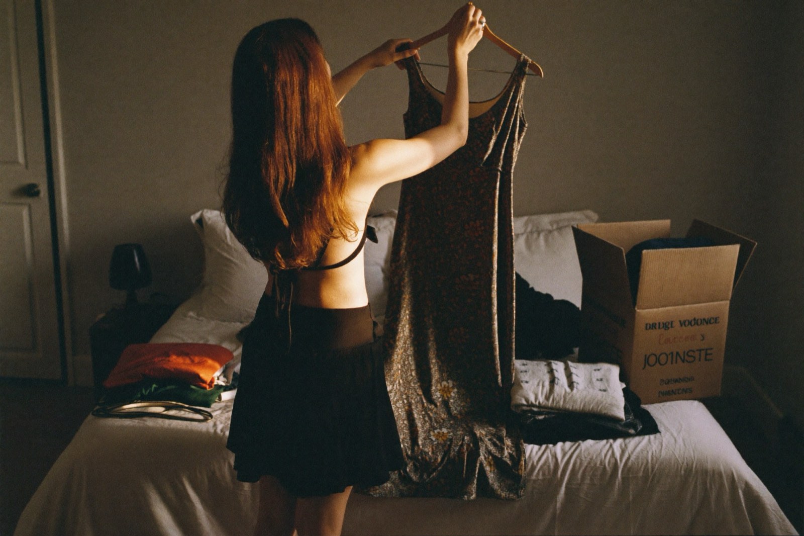 Woman holding a floral dress between a keep pile and a donate box while decluttering her sentimental closet